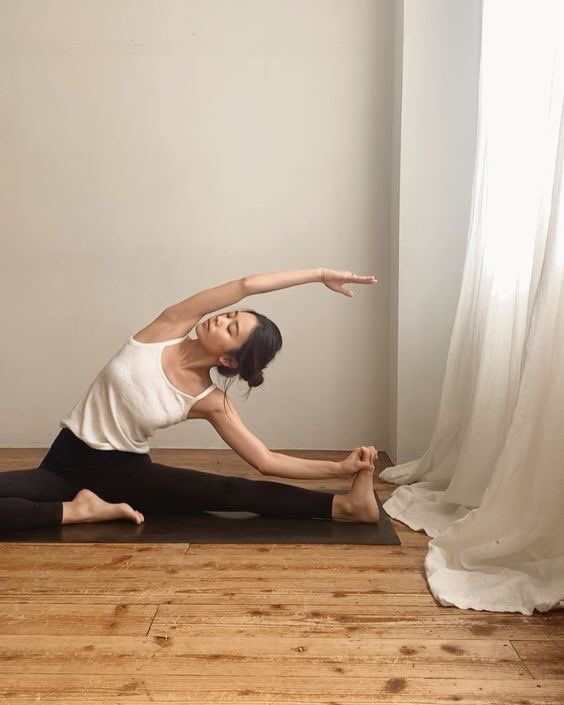 women doing a warm up stretch in yoga clothes with yoga mat, in a room with harwood floors and natural light